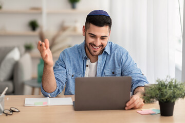Smiling israeli man having videochat on laptop computer at home - obrazy, fototapety, plakaty