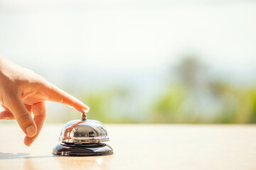 Woman ringing hotel bell of summer beach hotel front desk. Coastline sea and palm tree view. Travel...