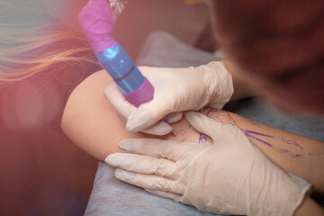 Master tattoo draws the red paint on the clients tattoo. Tattoo artist holding a pink tattoo machine in black sterile gloves and working on the professional blue mat.