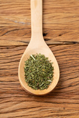Closeup of dried parsley on a spoon over wooden table