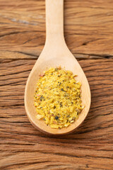 Closeup of lemon pepper seasoning on a spoon over wooden table