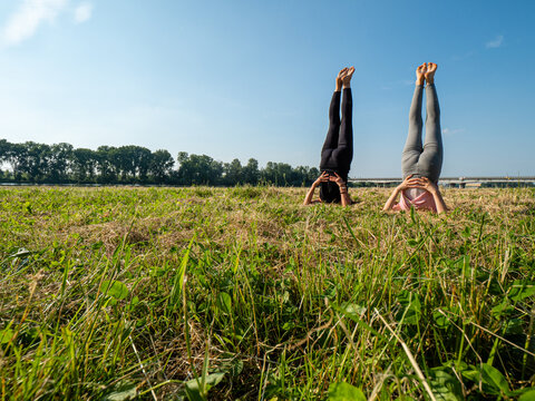 one adult fit woman teaches yoga to a girl at the coastside, summer, in a park