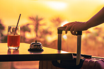 Woman with suitcase ringing hotel service bell with welcome drink and sea and palm tree view on...