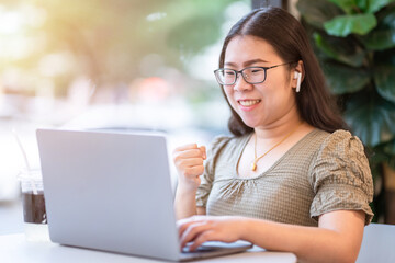 Happy successful business of asian freelance people business female wearing wireless earphonesexpressed confidence embolden working with laptop computer sitting in coffee shop like the background