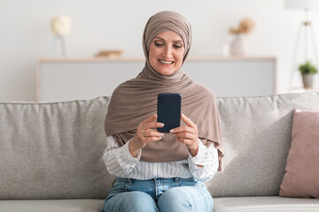 Happy Senior Muslim Woman Using Phone Browsing Internet At Home