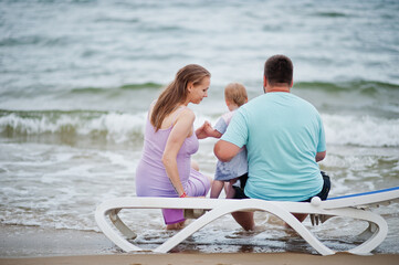 Summer vacations. Parents and people outdoor activity with children. Happy family holidays. Father, pregnant mother, baby daughter sitting on sunbed at sea sand beach.