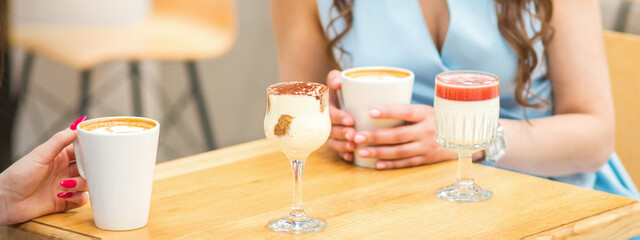 Hands of a young woman holding a cup of coffee with different cocktails on the table at the cafe.