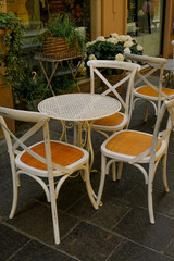 White wooden table with chairs across plants in pots in restaurant terrace. Cafe exterior. City life