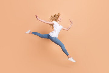 Fototapeta na wymiar Photo of shiny charming young lady wear white t-shirt smiling jumping high running looking empty space isolated beige color background