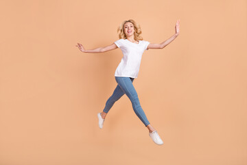 Fototapeta na wymiar Photo of adorable shiny young lady wear white t-shirt smiling jumping high running isolated beige color background