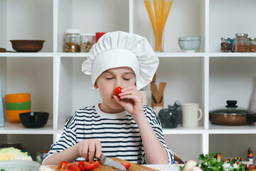 Little chef cutting fresh cherry tomatoes for salad. Kid want to be a professional chef. Cute boy cook healthy dinner for family.
