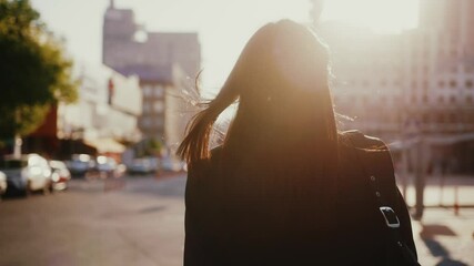 Following young tourist beautiful woman wearing black business jacket and bag, enjoying sunlight in big city, walking down the street. - Powered by Adobe