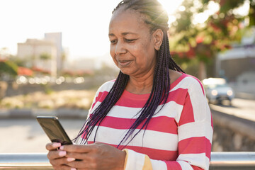 African american senior woman using mobile phone in the city - Sunset in background - Powered by Adobe