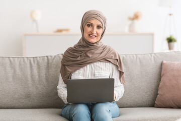 Happy Senior Muslim Lady Using Laptop At Home, Wearing Hijab