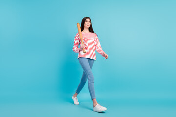 Full length body size view of attractive confident cheery girl walking carrying bat isolated over bright blue color background
