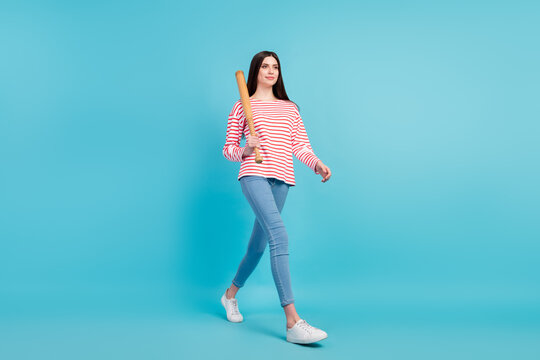 Full length body size view of attractive confident cheery girl walking carrying bat isolated over bright blue color background