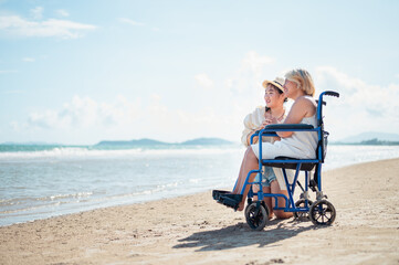 Grandchildren sit with the neighborhood on a wheelchair relaxing on the beach.