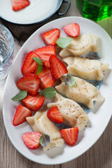 Cottage cheese dumplings served with fresh strawberries on a white oval plate, vertical shot, closeup