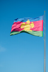 The flag with the coat of arms of the Krasnodar Territory flutters in the wind against the blue sky.