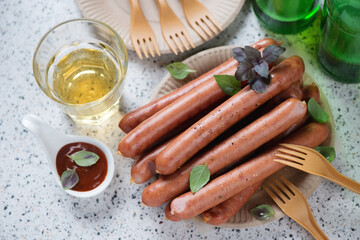 Pile of smoked sausages on a carton plate with dip sauce and beer, high angle view on a beige granite background, studio shot