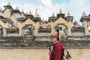 Fototapeta na wymiar Portrait Asian man backpacker travel pagoda in southeast Asia. Traveler look up face happiness wearing a hat carrying a backpack on a Buddhist temple.