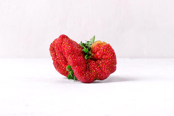 Weird looking strawberry. Imperfect but tasty farmer product on white table. Fighting food waste 