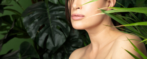 Beautiful woman with flawless fresh clean skin amongst fresh green tropical leaf fronds. Natural...