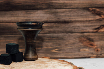 An earthenware bowl for a hookah with coconut coals stands on a wooden background.