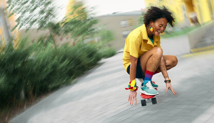 African American woman with vitiligo delighted with skateboarding on modern city street. Blurred...