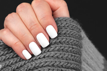 Female hand with gray knitted scarf with beautiful manicure - white nails. Nail care concept