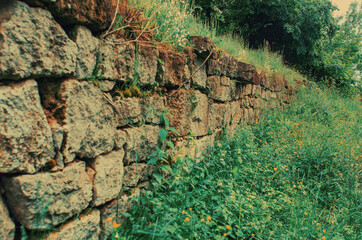 An old abandoned stone wall made of old stones overgrown with grass and moss