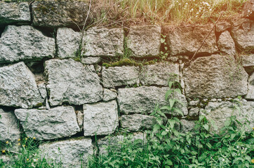 An old abandoned stone wall made of old stones overgrown with grass and moss