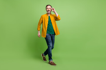 Full length photo of positive mature cheerful man walk step wear glasses isolated on green color background