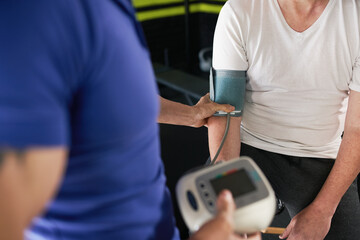 Close up of unrecognizable trainer measuring senior, elderly man's blood pressure