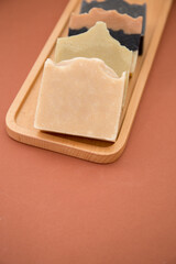 Assorted natural soaps on wooden tray isolated on brown
