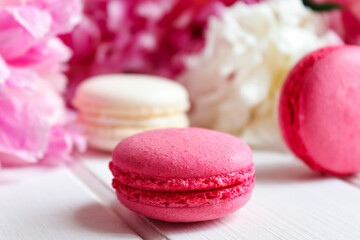 Macarons and peonies close-up on a white wooden table. Selective focus. Bakery and floral background