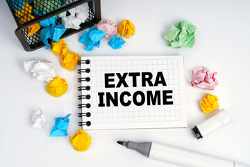 On the table is a basket, multi-colored paper and a notebook with the inscription - Extra Income