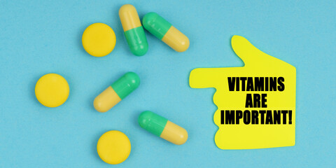 On a blue background, there are pills and a hand-sticker with the inscription - Vitamins are important
