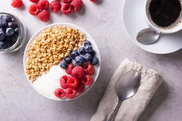 Breakfast consisting of plain yogurt garnished with berries and granola oatmeal beside a cup of coffee