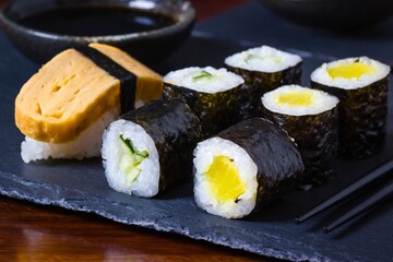 Homemade vegetarian maki sushi on slate plate with chopsticks and soy sauce bowl in the back