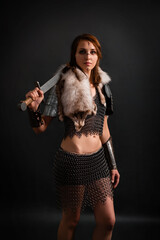 Portrait of a medieval woman warrior in chain mail armor and polar fox fur on her shoulders standing with a sword in hand on a dark background.  Female warrior silhouette.