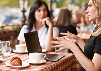 Beautiful women workers or students using laptop at cafe and talking