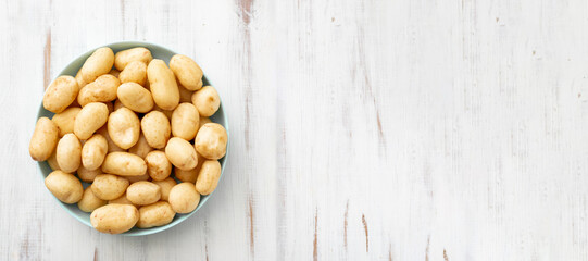 Young raw potatoes small on a plate on a white wooden background. Banner. Place for your text.
