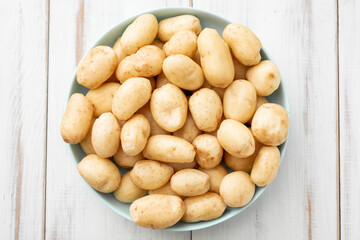 Young raw potatoes small on a plate on a white wooden background.