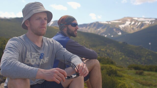 Portrait of two men are sitting on a stone in the mountains. They look ahead. Rest time on the rise. Restoring the forces of the tourist. Shaking the camera.