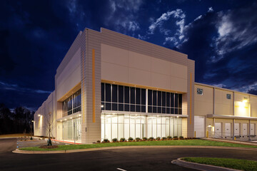 Large lit generic white industrial storage warehouse façade at night dusk