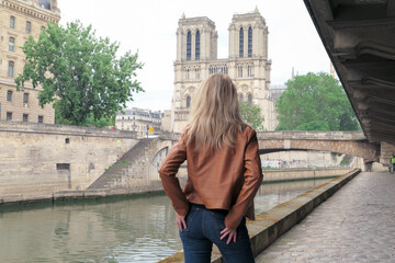 Blonde woman in trousers, standing from behind on the banks of the banks of the Seine. Cathedral of...