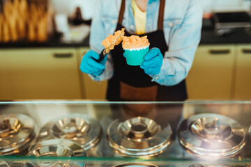 Young and happy saleswoman in black apron selling handmade ice cream at the counter of the pastry shop.
