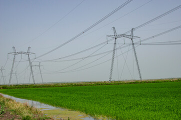High voltage electricity line against the background of the sky and green field.