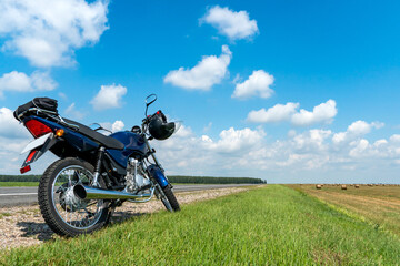 Fototapeta na wymiar A motorcycle trip through the countryside in the summer. A blue motorcycle on a background of blue sky and white clouds.